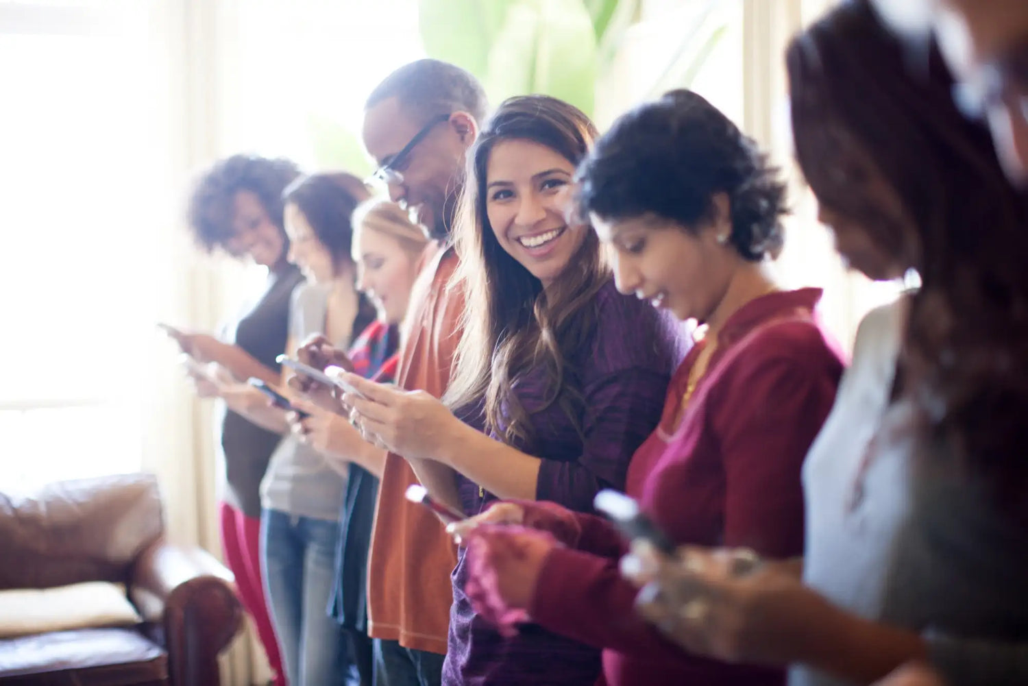 A group of people standing in a line, each holding and looking at their own smartphone.